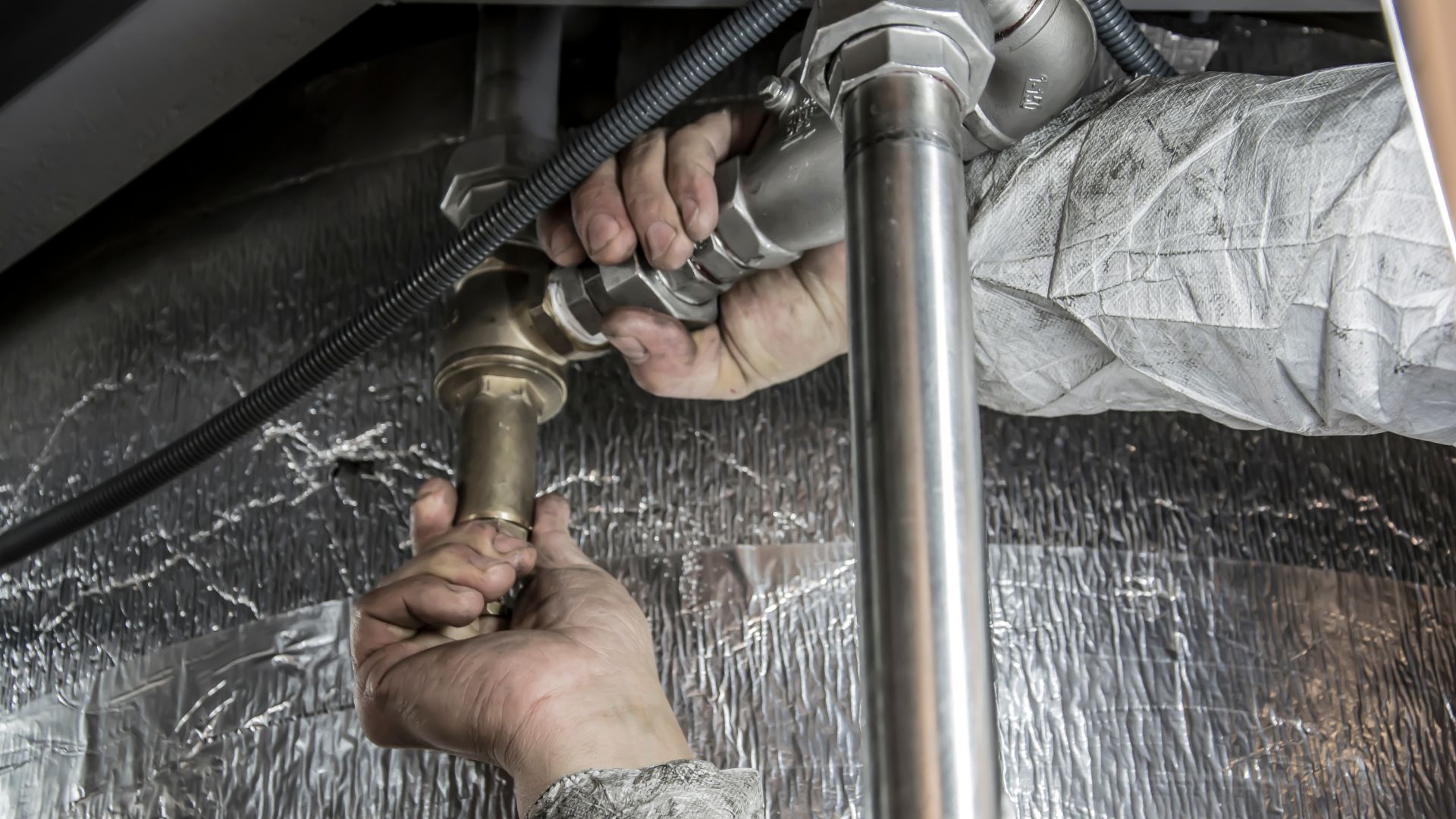 A man fixing a water heater with a hose