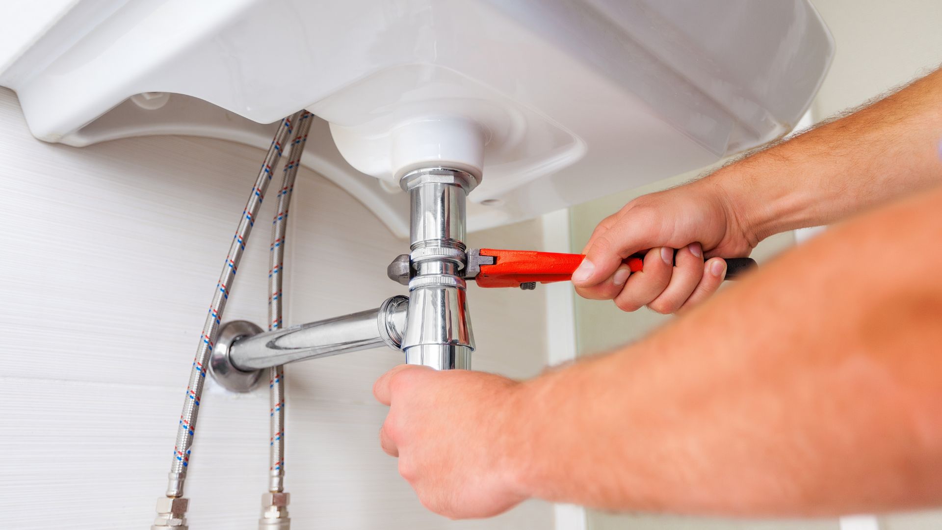 A man fixing a bathroom sink with a wrench